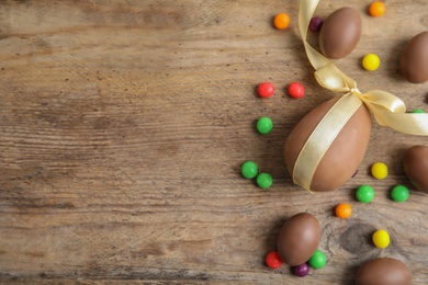 Tasty chocolate eggs and colorful candies on wooden table, flat lay. Space for text