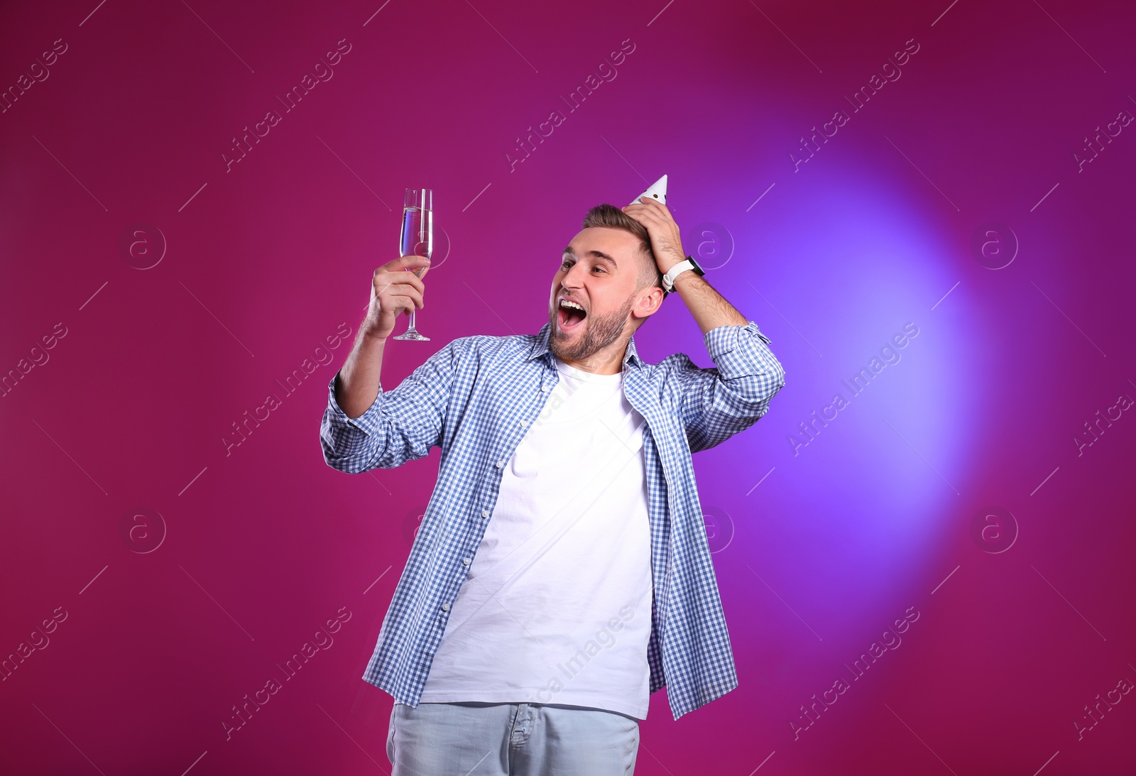 Photo of Portrait of happy man with party cap and champagne in glass on color background