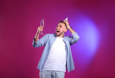 Portrait of happy man with party cap and champagne in glass on color background