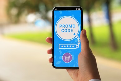 Photo of Woman holding smartphone with promo code outdoors, closeup