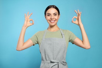Young woman in grey apron on light blue background,