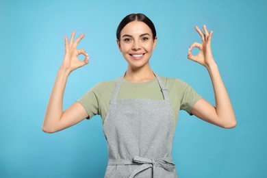 Photo of Young woman in grey apron on light blue background,