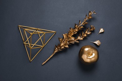Golden dried flower, decorative pyramid and apple on black background, flat lay