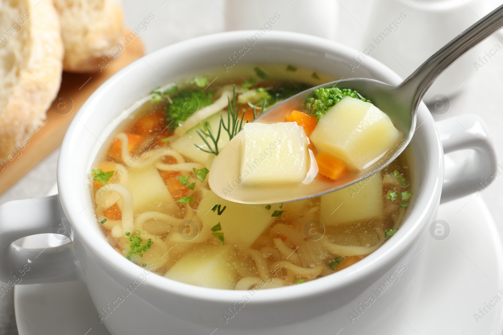 Photo of Spoon of fresh homemade vegetable soup over full dish on table, closeup