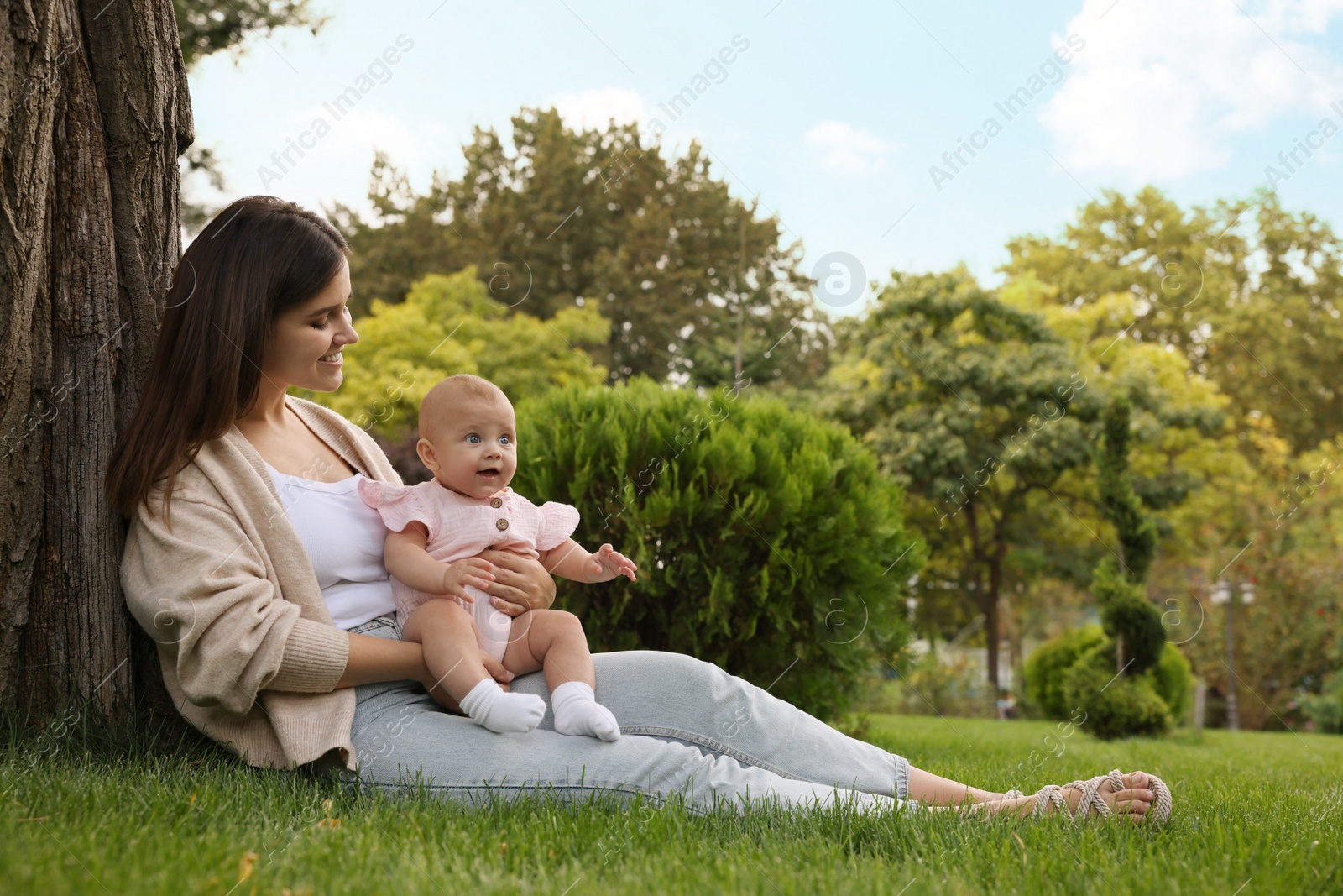 Photo of Happy mother with adorable baby sitting on green grass in park