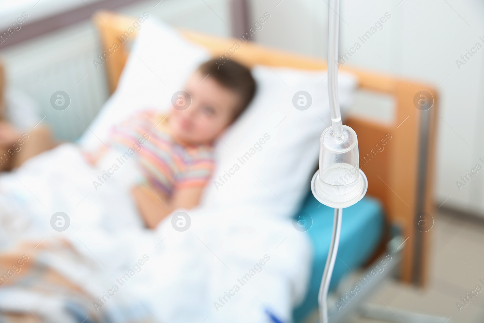 Photo of Little child with intravenous infusion in hospital bed, focus on drip chamber