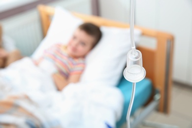 Photo of Little child with intravenous infusion in hospital bed, focus on drip chamber