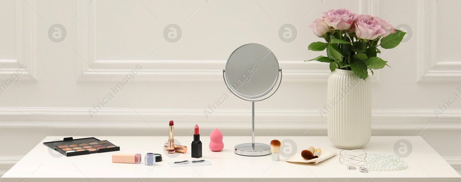 Image of Makeup room. Mirror, cosmetic products, jewelry and vase with pink roses on white dressing table indoors, banner design