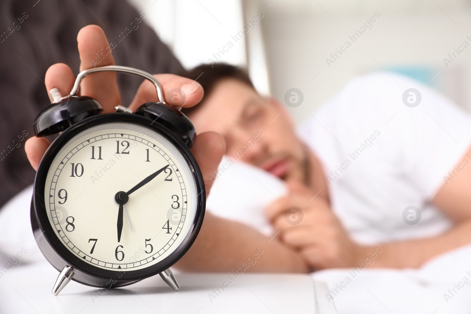 Photo of Sleepy man turning off alarm clock on nightstand. Bedtime