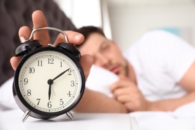 Sleepy man turning off alarm clock on nightstand. Bedtime