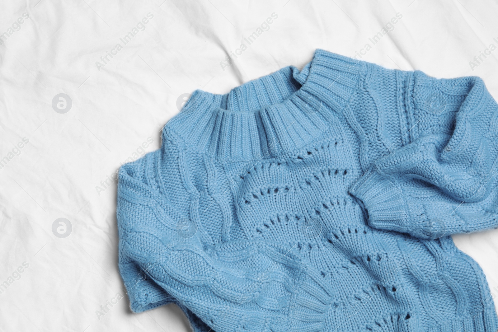 Photo of Blue knitted sweater on white fabric, flat lay
