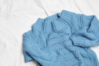 Blue knitted sweater on white fabric, flat lay