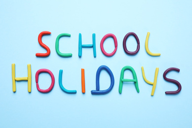 Photo of Phrase School Holidays made of modeling clay on light blue background, top view