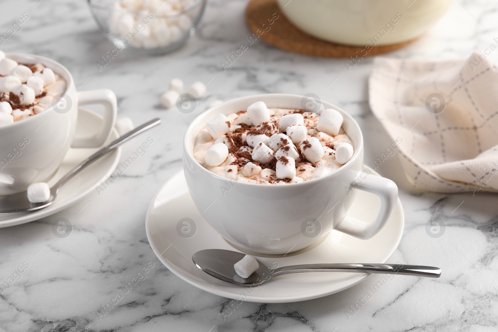 Photo of Aromatic hot chocolate with marshmallows and cocoa powder served on white marble table, closeup