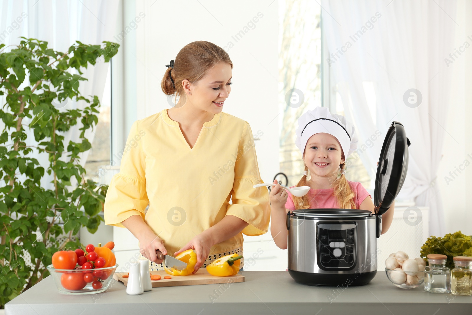 Photo of Mother and daughter preparing food with modern multi cooker in kitchen