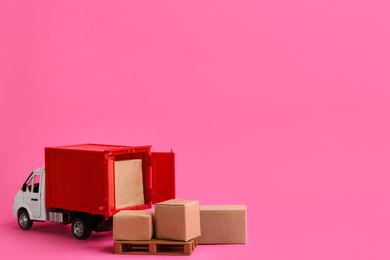 Photo of Truck model and carton boxes on pink background, space for text. Courier service