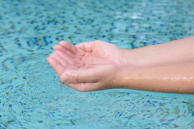 Girl holding water in hands above pool, closeup