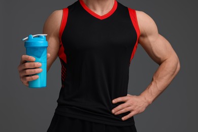 Young man with muscular body holding shaker of protein on grey background, closeup