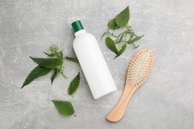 Photo of Stinging nettle, cosmetic product and brush on grey background, flat lay. Natural hair care