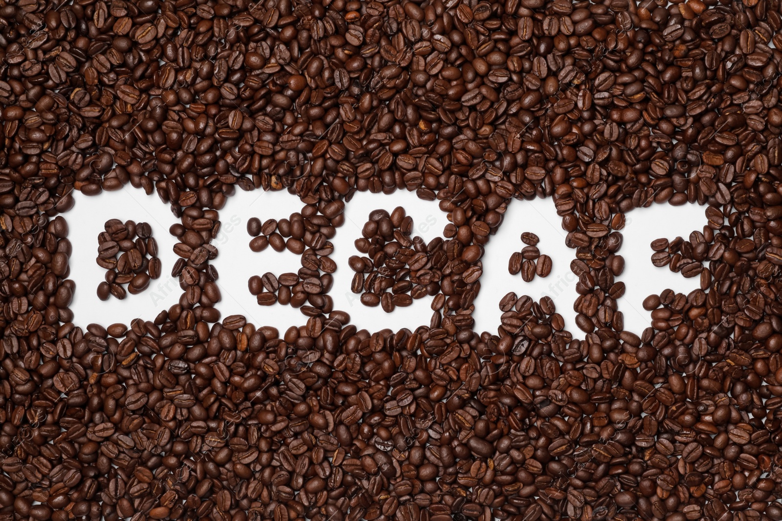 Photo of Word Decaf in coffee beans on white background, top view