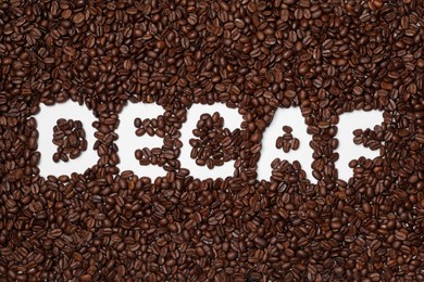 Photo of Word Decaf in coffee beans on white background, top view