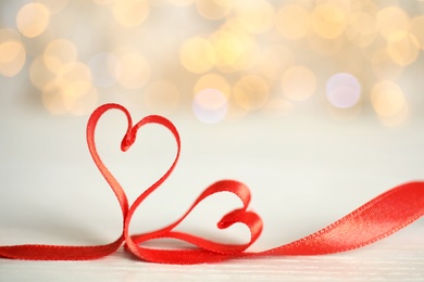 Photo of Two hearts made of red ribbon on table against blurred lights, space for text. St. Valentine's day card