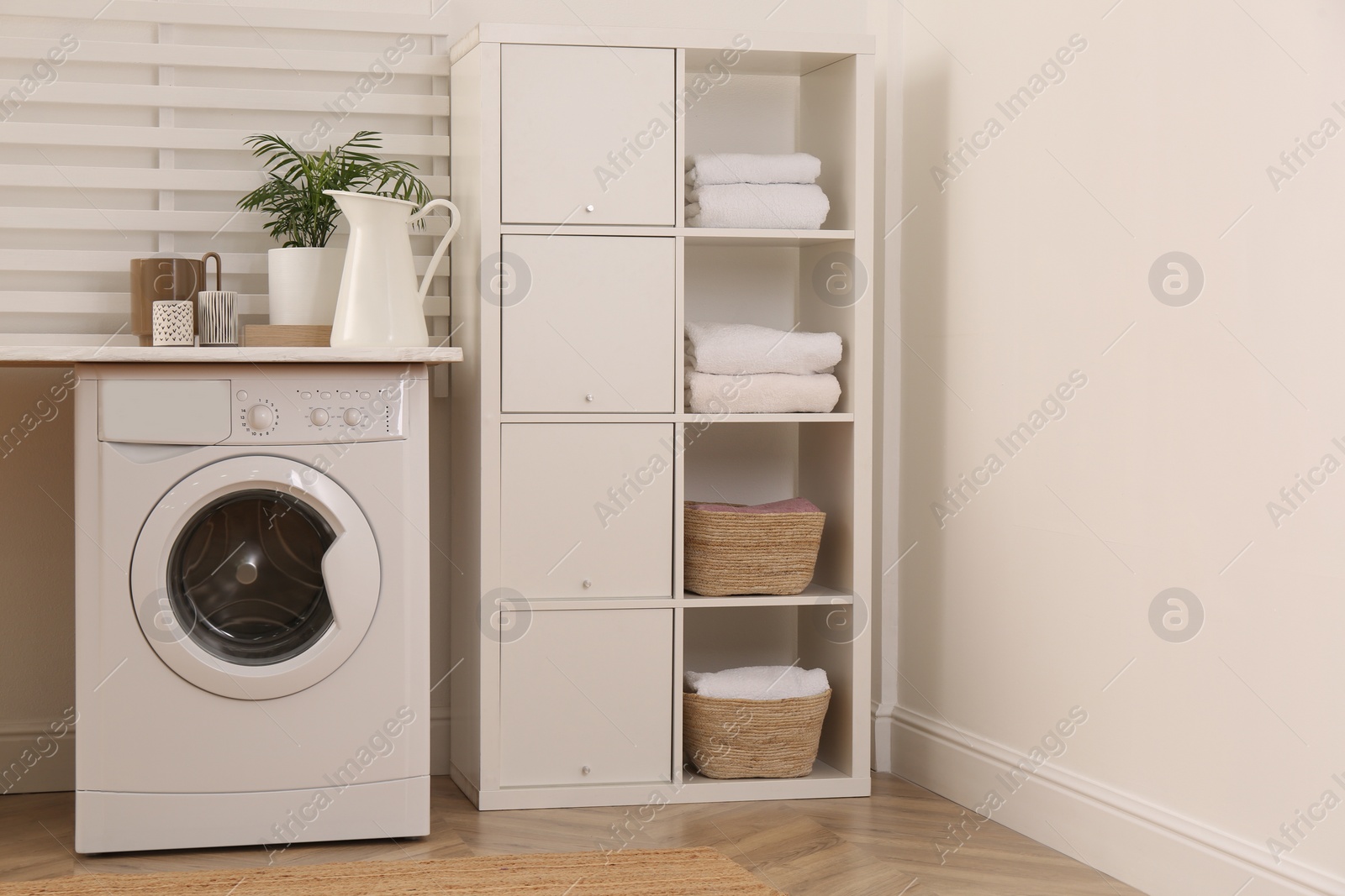 Photo of Laundry room interior with modern washing machine and shelving unit near white wall