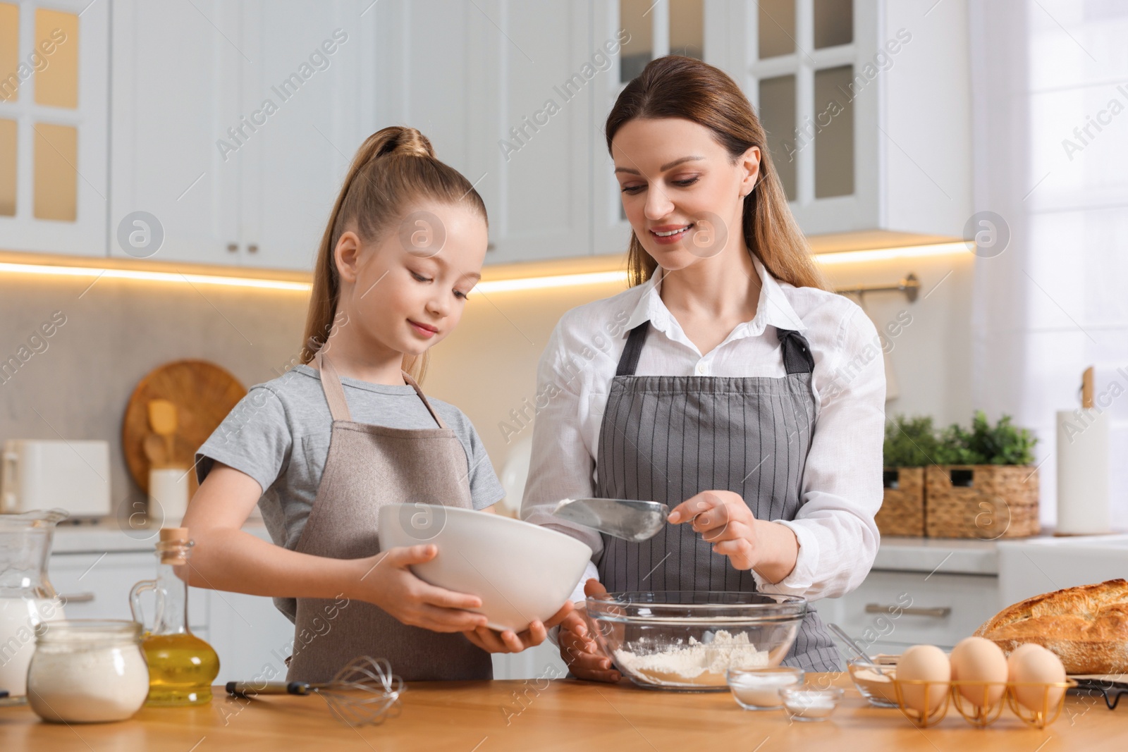 Photo of Making bread. Mother and her daughter preparing dough at wooden table in kitchen