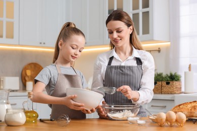 Photo of Making bread. Mother and her daughter preparing dough at wooden table in kitchen