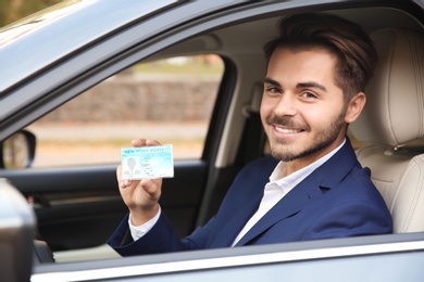 Photo of Young man holding driving license in car