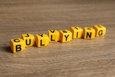 Photo of Word Bullying made of yellow cubes with letters on wooden table, closeup