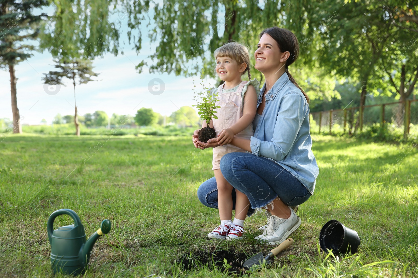 Photo of Mother and her daughter planting tree together in garden, space for text