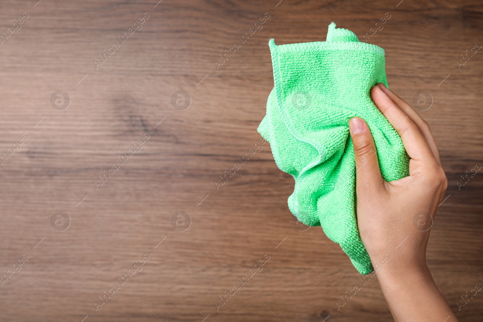 Photo of Woman with microfiber cloth on wooden background, closeup. Space for text