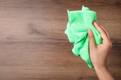 Photo of Woman with microfiber cloth on wooden background, closeup. Space for text