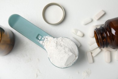 Measuring scoop of amino acids powder and pills on white table, flat lay