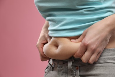 Photo of Woman touching belly fat on pink background, closeup. Overweight problem