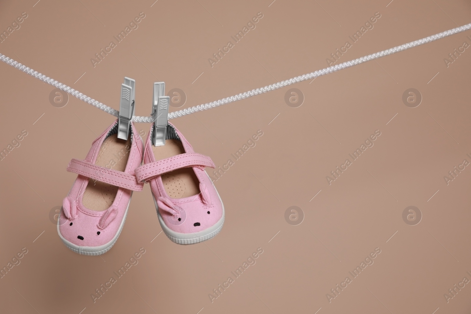 Photo of Cute small baby shoes hanging on washing line against brown background, space for text