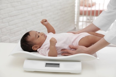 Doctor weighting African-American baby on scales in light room
