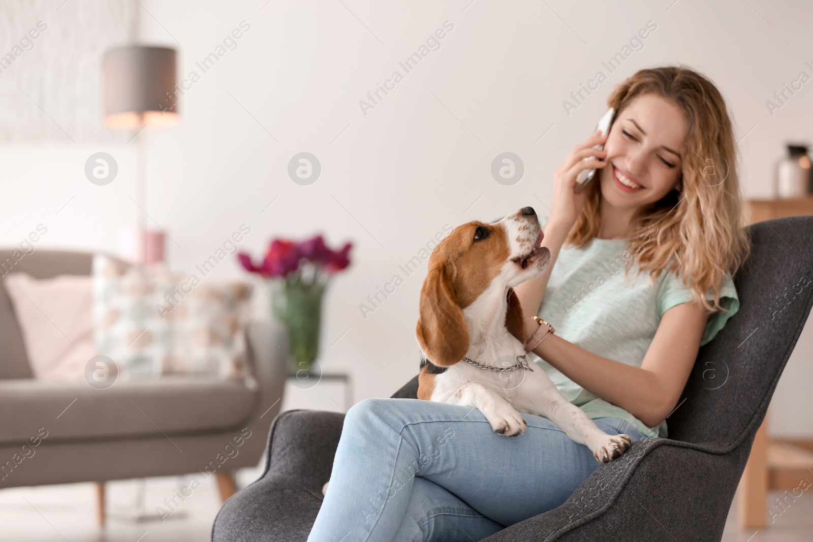 Photo of Young woman talking on phone while stroking her dog at home