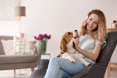 Photo of Young woman talking on phone while stroking her dog at home