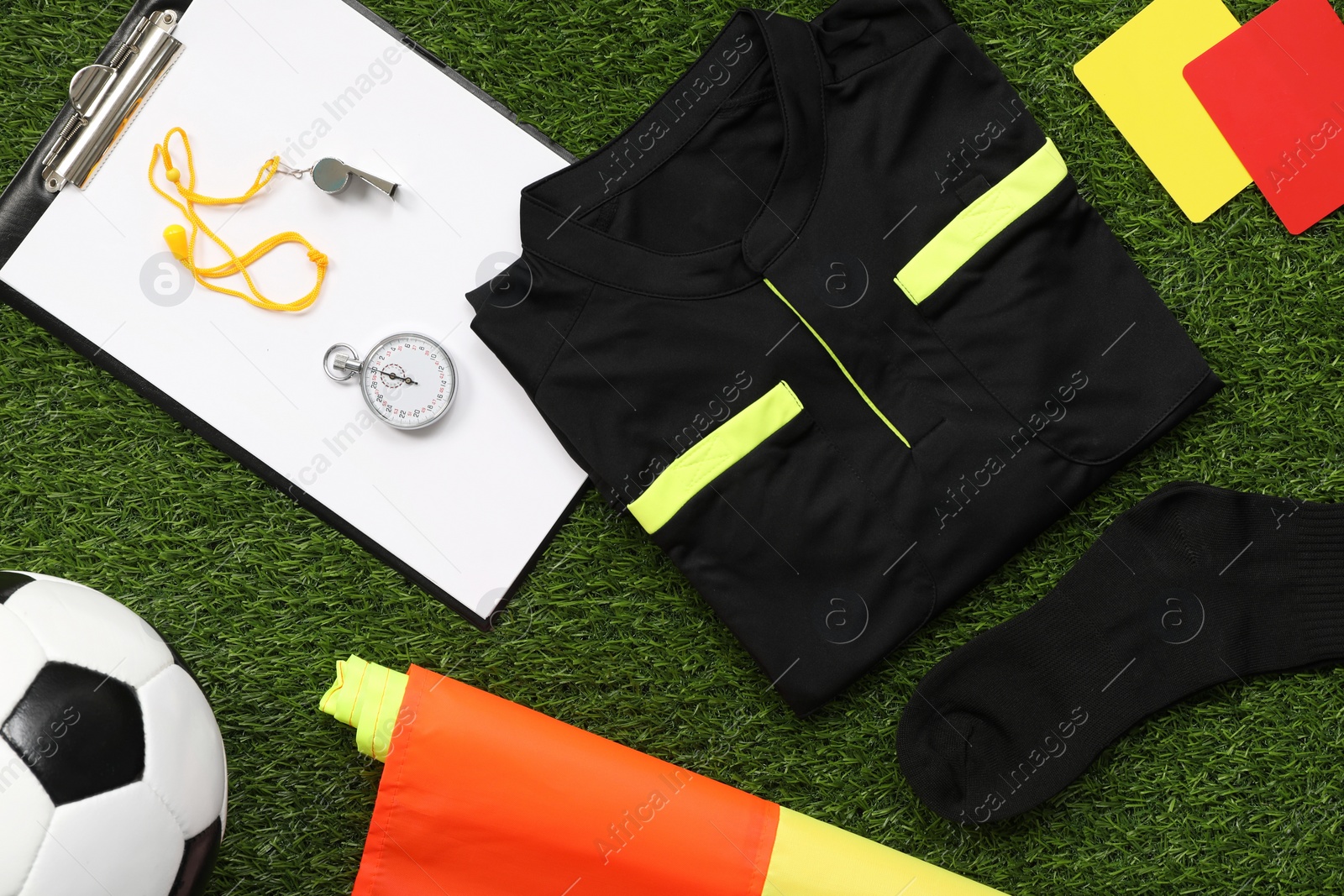 Photo of Uniform, soccer ball and other referee equipment on green grass, flat lay