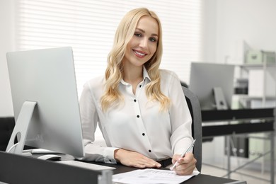 Happy secretary with pen at table in office