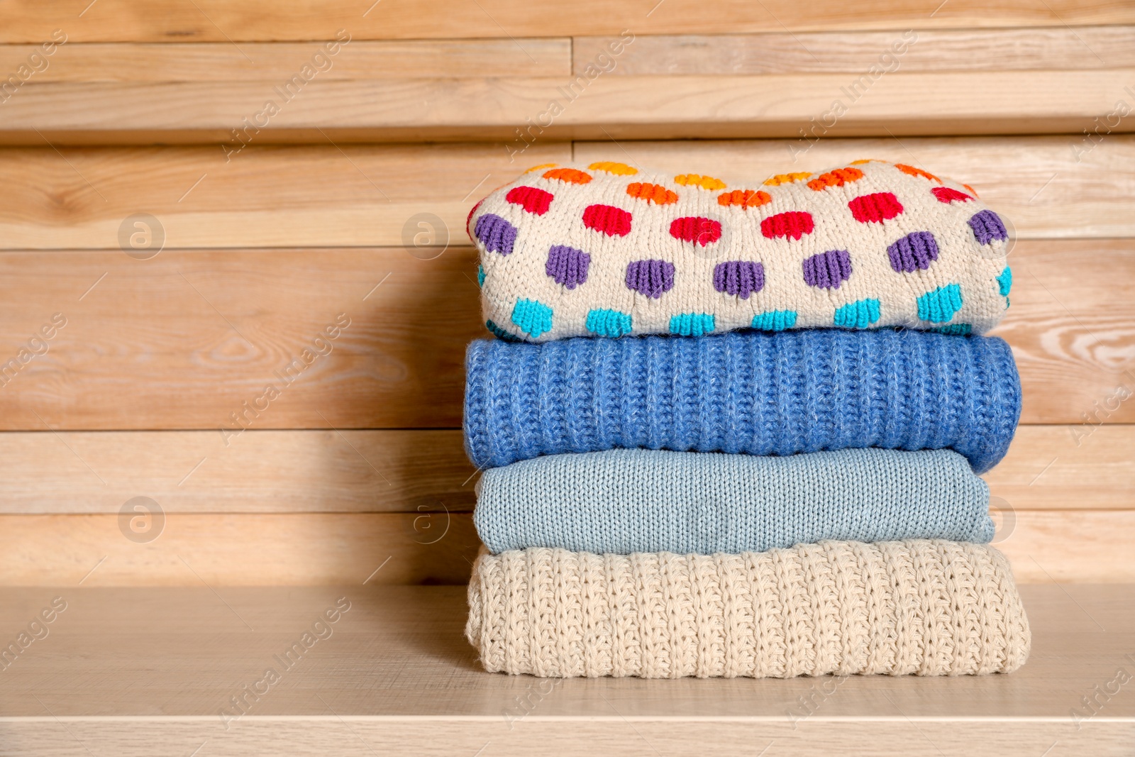 Photo of Stack of winter clothes against wooden background. Space for text