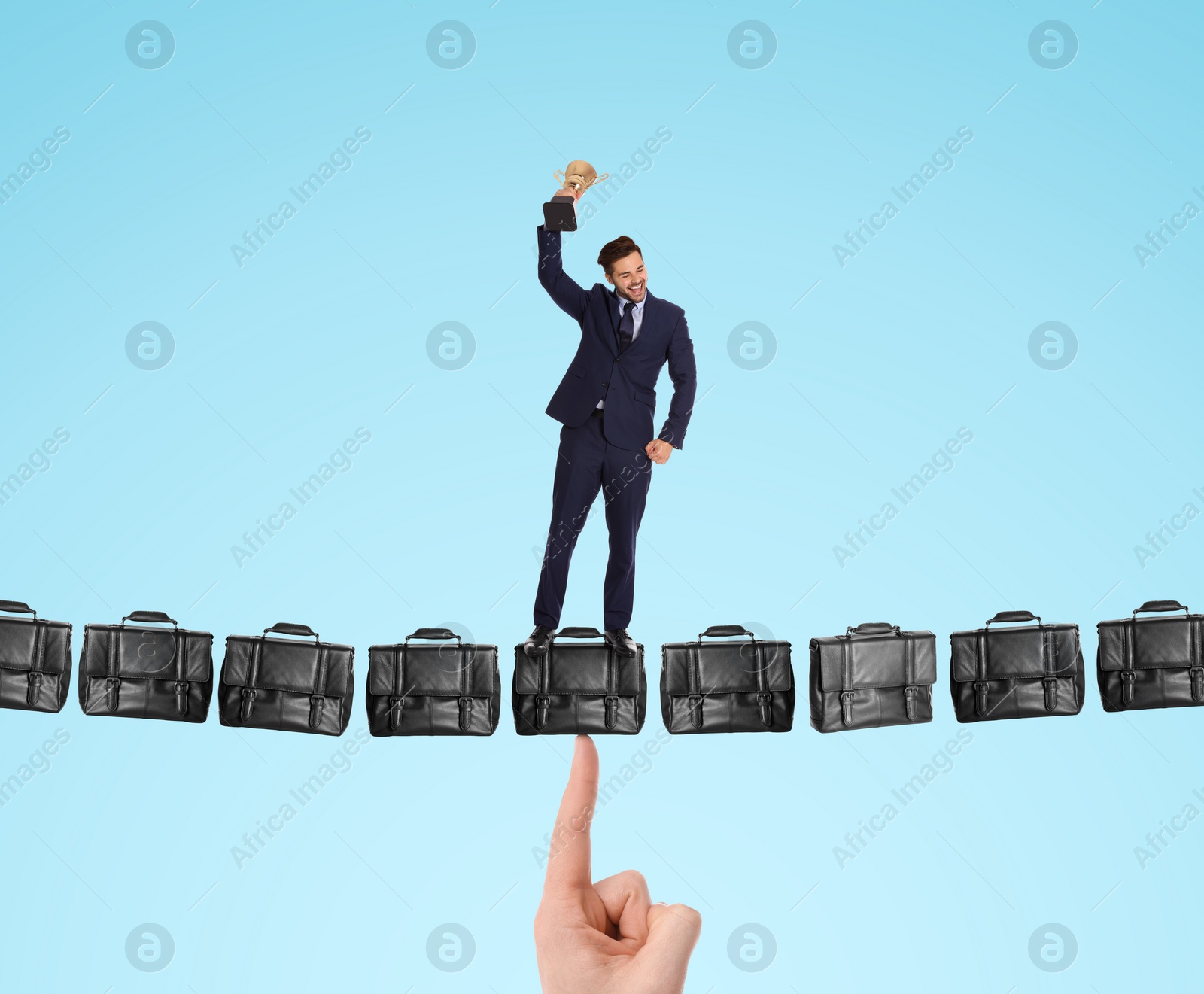 Image of Happy businessman with gold trophy cup standing on hanging bridge made of leather briefcases against light blue background. Bag supported by someone's finger