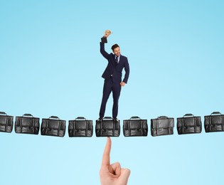 Happy businessman with gold trophy cup standing on hanging bridge made of leather briefcases against light blue background. Bag supported by someone's finger