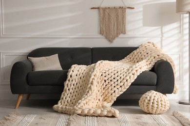 Photo of Soft chunky knit blanket on sofa in living room. Interior design