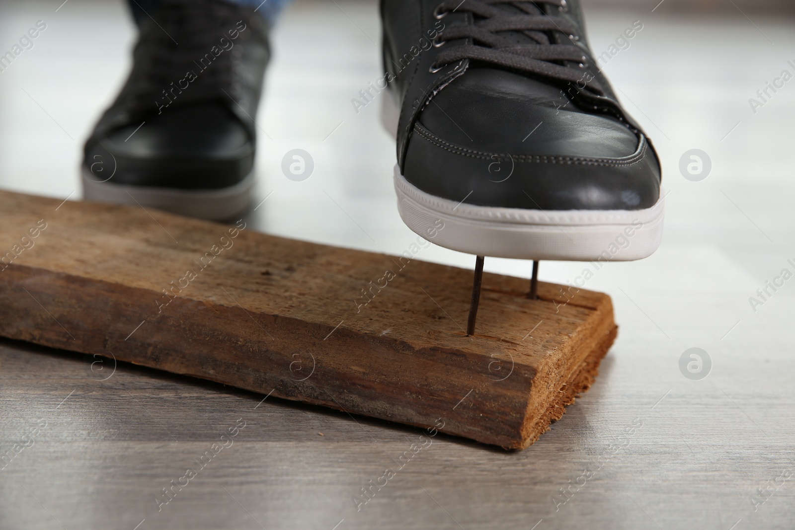 Photo of Careless man stepping on nails in wooden plank, closeup