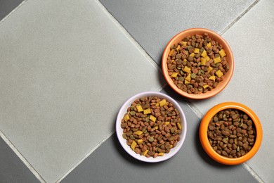 Photo of Pet bowls with dry food on floor, flat lay. Space for text