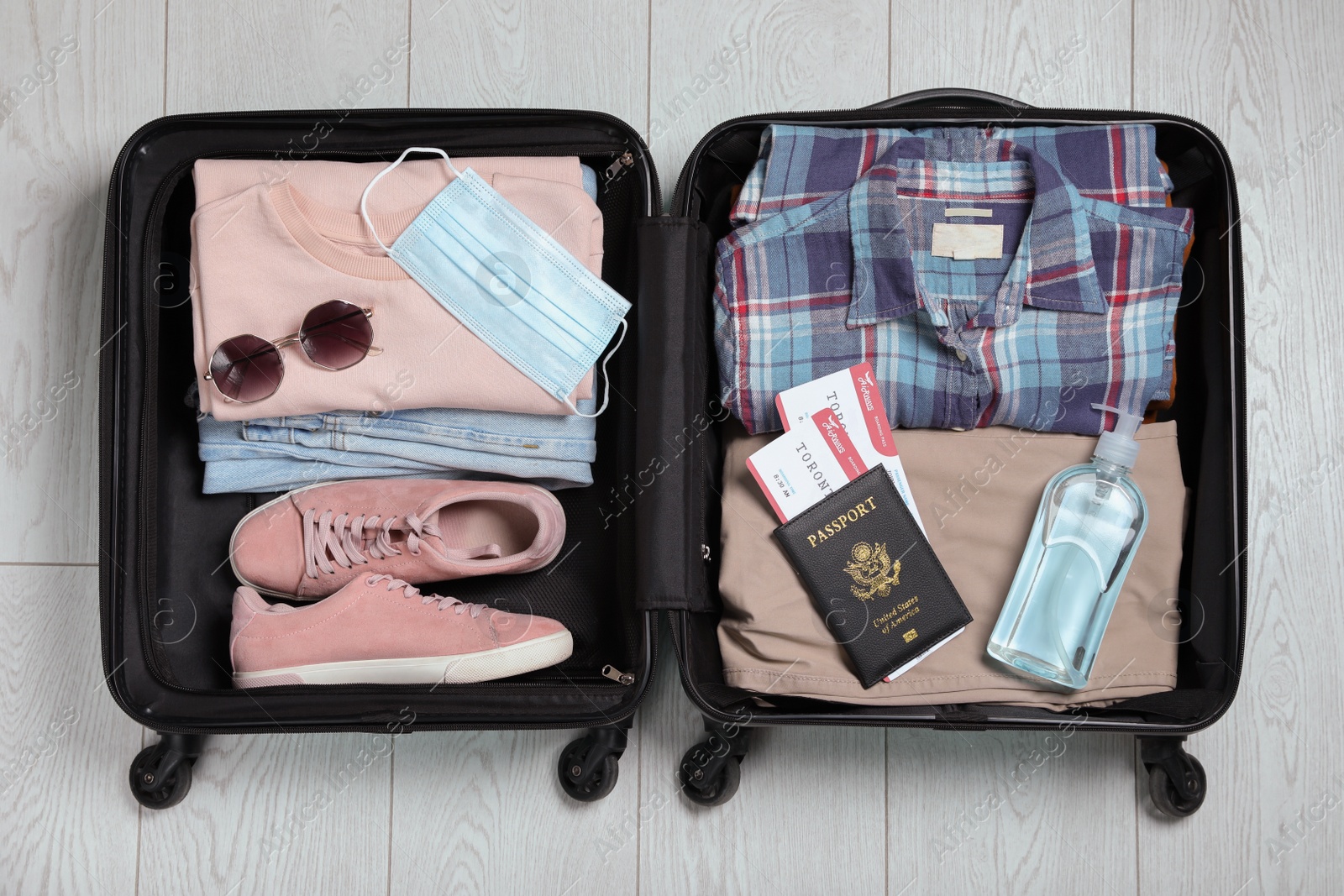 Photo of Open suitcase with passport, tickets, sanitizer and protective mask on wooden floor, top view. Travel during quarantine