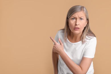 Photo of Surprised senior woman pointing at something on beige background, space for text